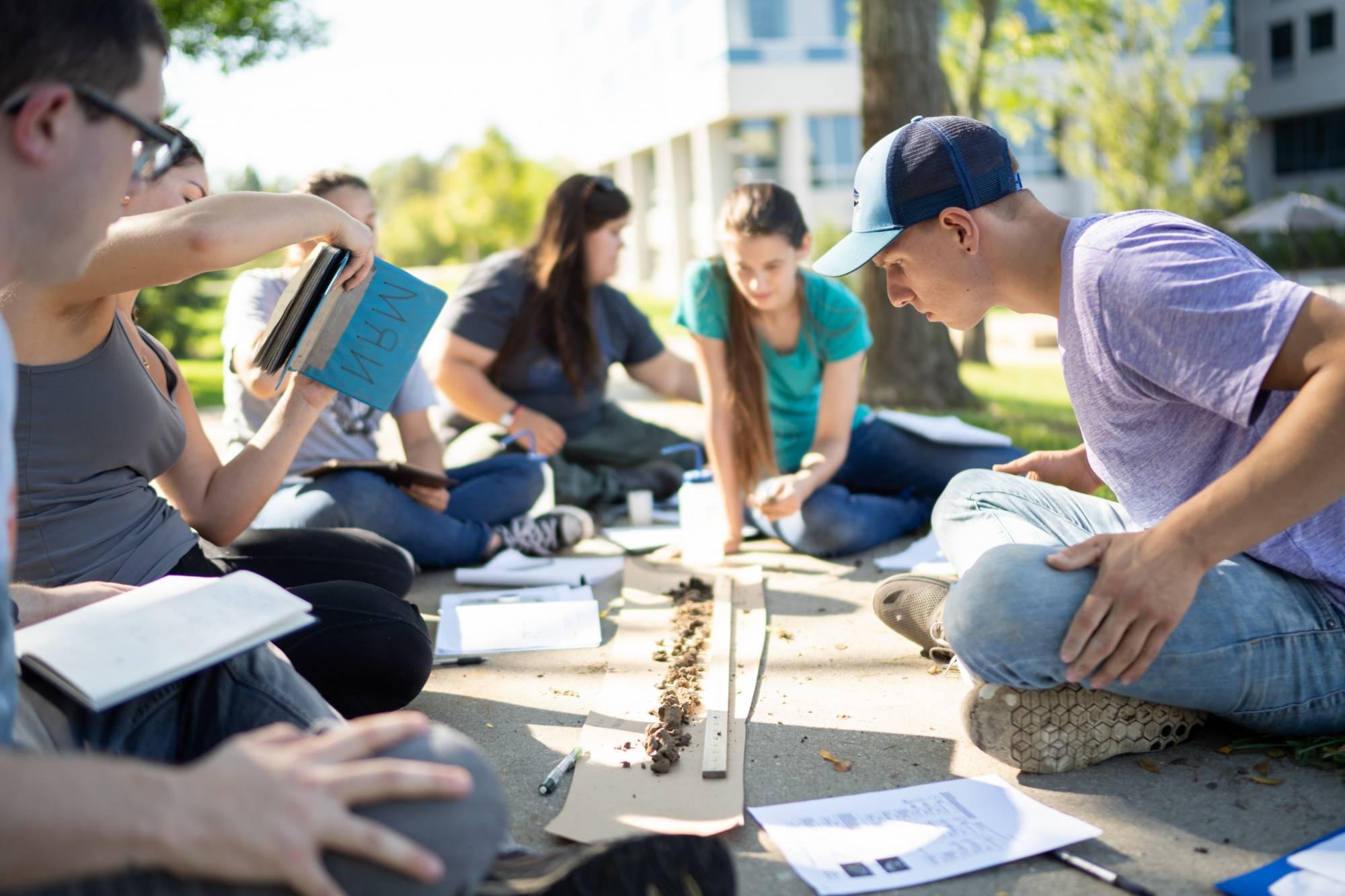 坐在室外地面上的学生们聚集在一个土壤样本周围，并对其进行分析
